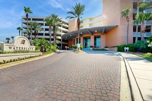 A hotel entrance with a sign reading "WATERSCAPE," paved walkway, palm trees, and a multi-story building with balconies. - 4th Floor Cozy, Welcoming Condo At Waterscape Waterfall, Lazy River (Fort Walton Beach)