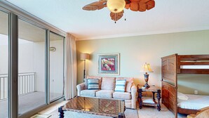 Un salon comprenant un canapé, une table basse, une lampe, un lit et un ventilateur de plafond.