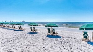 Une plage bordée de rangées de parasols verts et de chaises longues en bois.