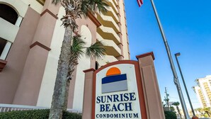 Un senyal per a Sunrise Beach Condominium amb un edifici al fons.