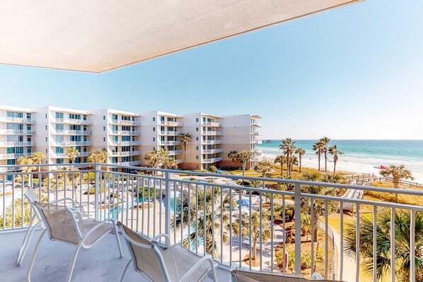 Ein Balkon mit Blick auf einen Strand, Palmen und einen Poolbereich.