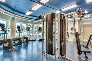 Ein Fitnessstudio mit unterschiedlichen Trainingsgeräten, darunter Laufbändern und Kraftmaschinen, und großen Fenstern, die für natürliches Licht sorgen.