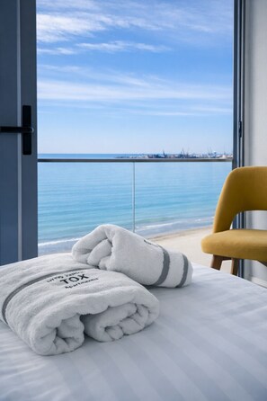A room with a bed, a yellow chair, and a view of the sea. - Sea view luxury duplex (Durrës)