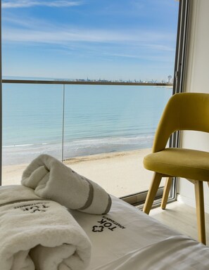 A room with a bed, a yellow chair, and a view of the beach and ocean. - Sea view luxury duplex (Durrës)