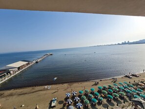 A beach with umbrellas and lounge chairs, a pier extending into the water, and a city skyline in the distance. - Sea view luxury duplex (Durrës)