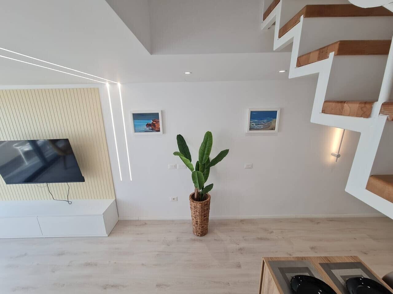 Ein modernes Wohnzimmer mit einem an der Wand befestigten Flachbildfernseher, einer großen Topfpflanze und einer Treppe mit Holzbodenstufen.