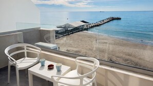 A balcony with two white chairs and a table, overlooking a beach and a pier.