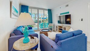 A modern living room with blue sofas, a glass coffee table, a lamp, and a TV. - Bright, beachy condo At Waterscape w children's playground, 2 hot tubs (Fort Walton Beach)