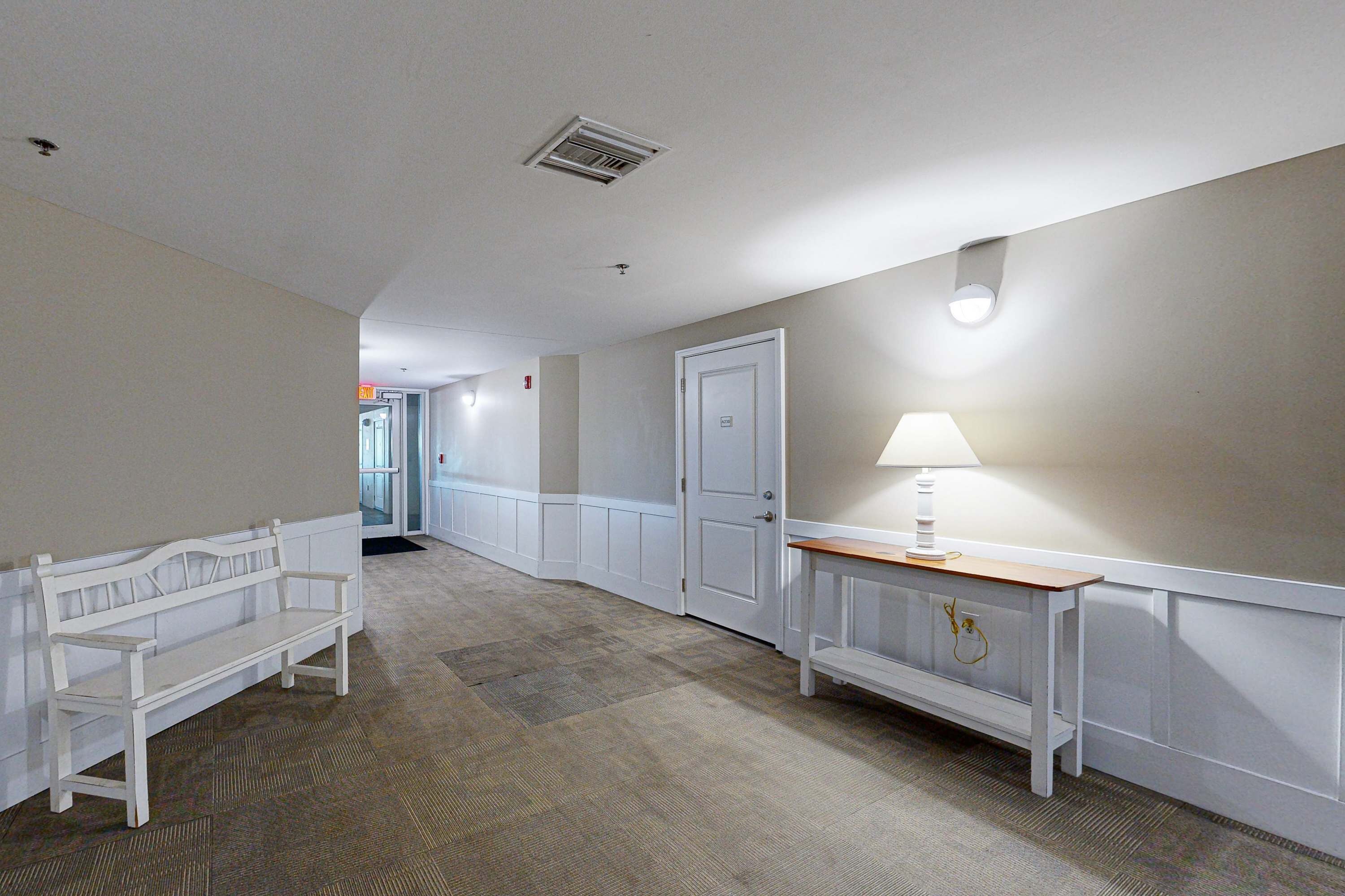 Un couloir avec un banc, une porte et une table sur laquelle se trouve une lampe.