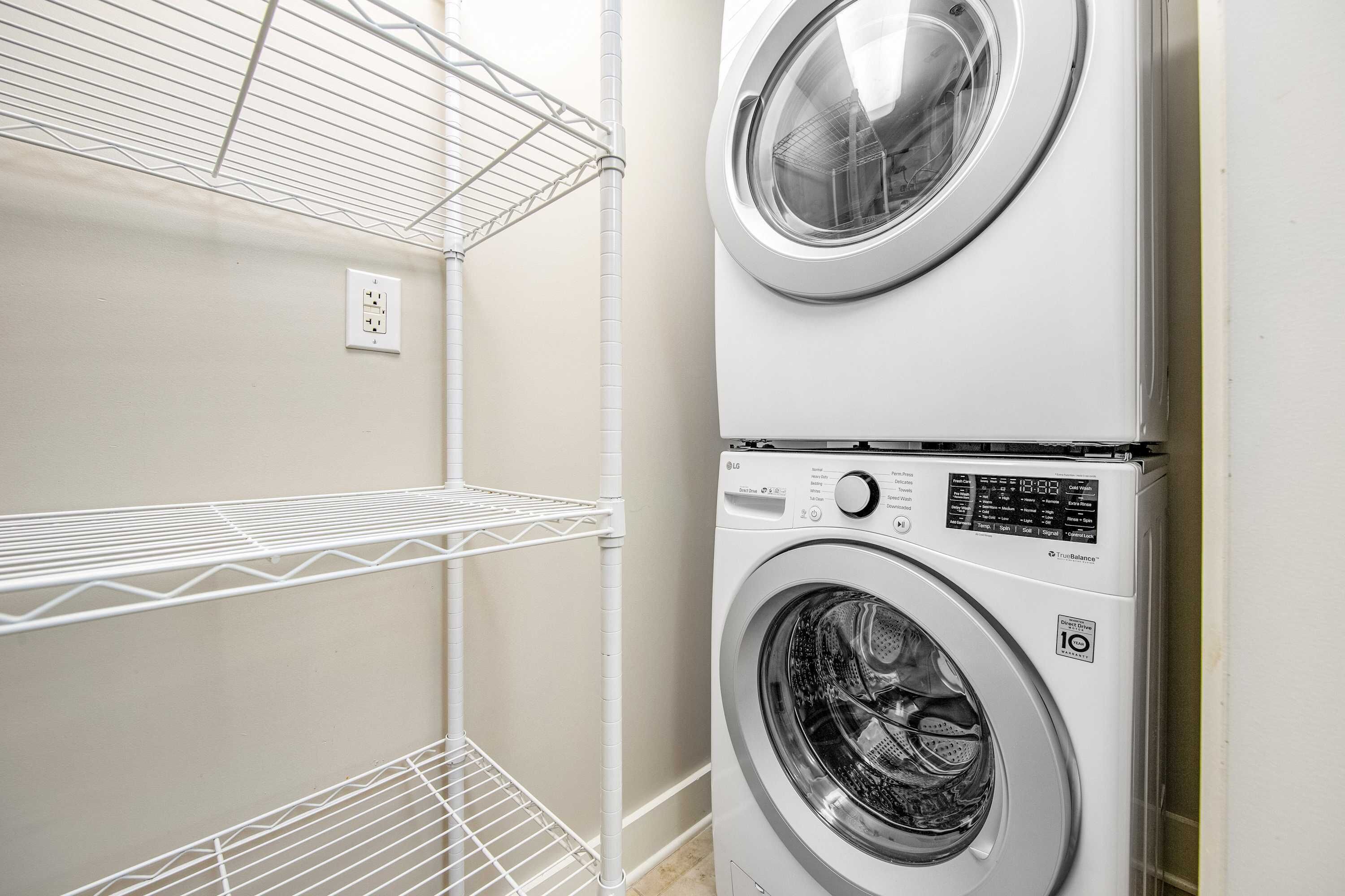 A laundry room with two stacked washing machines and metal shelving units.
