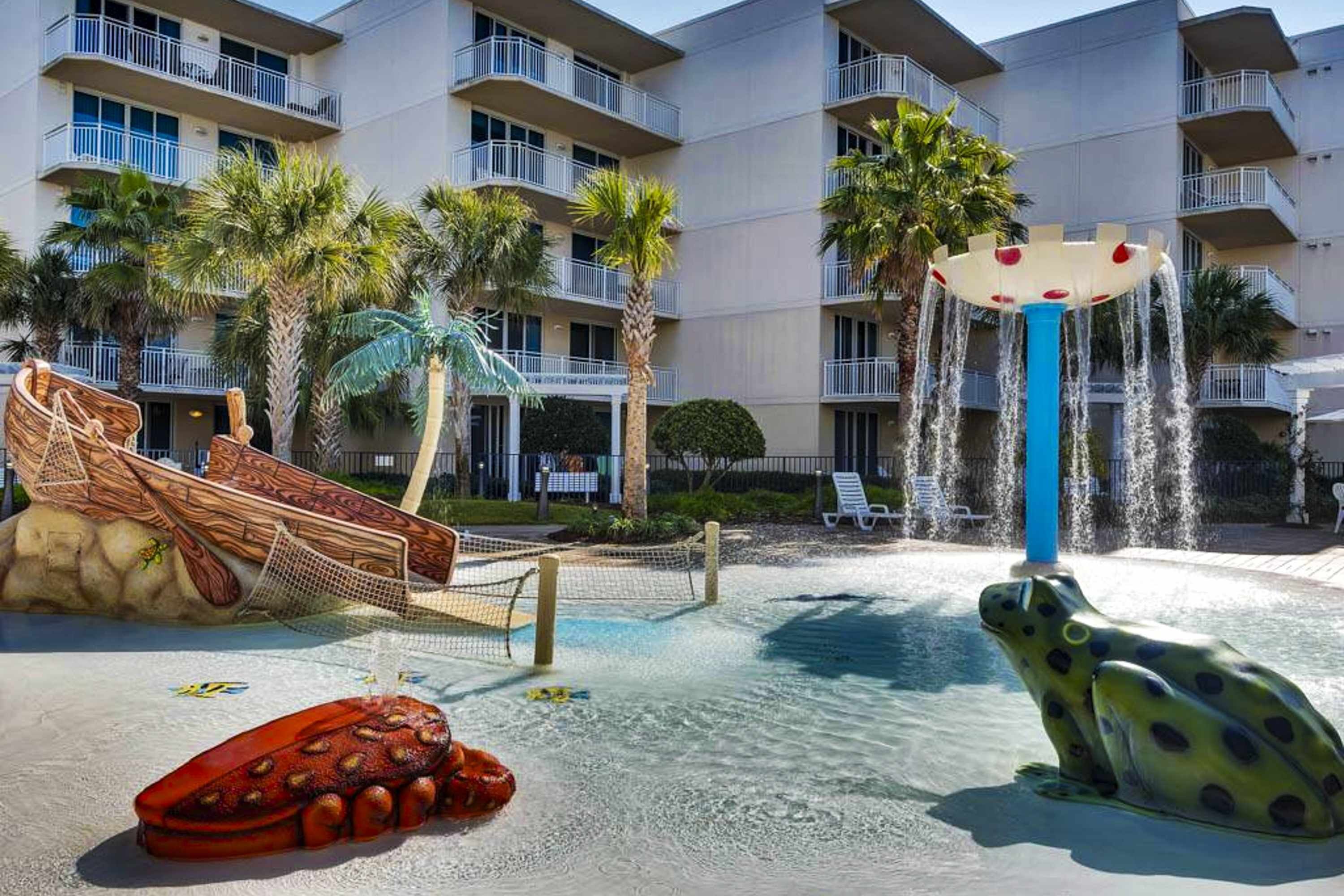 A water park with a slide, a frog-shaped water feature, and palm trees.
