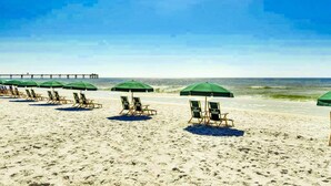 A beach with rows of beach chairs and umbrellas, a pier in the background, and the ocean. - 3rd Floor Picturesque Condo On Okaloosa Island Waterfall, Lazy River (Fort Walton Beach)