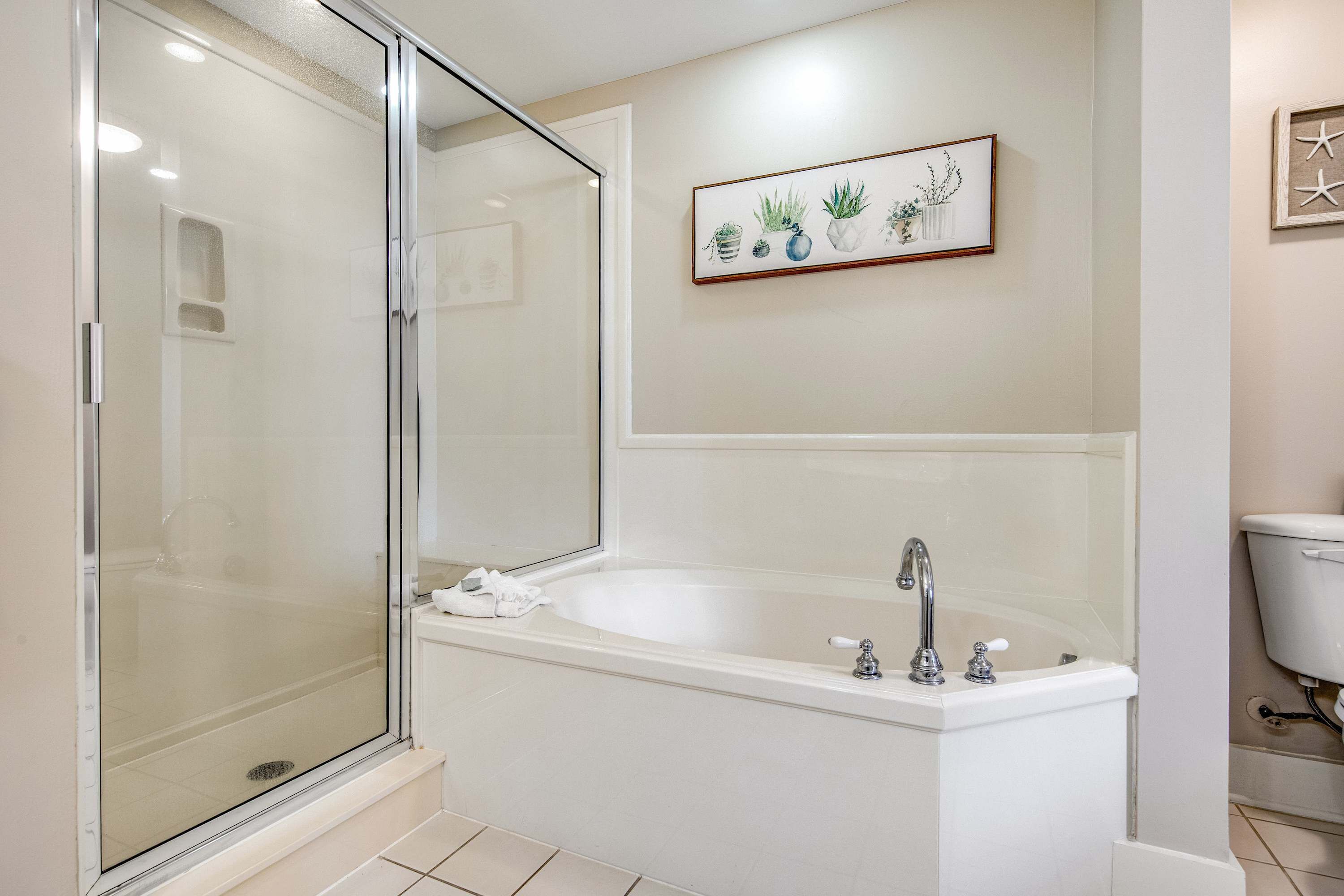 A modern bathroom with a glass-enclosed shower, a freestanding bathtub, and a framed plant artwork on the wall.