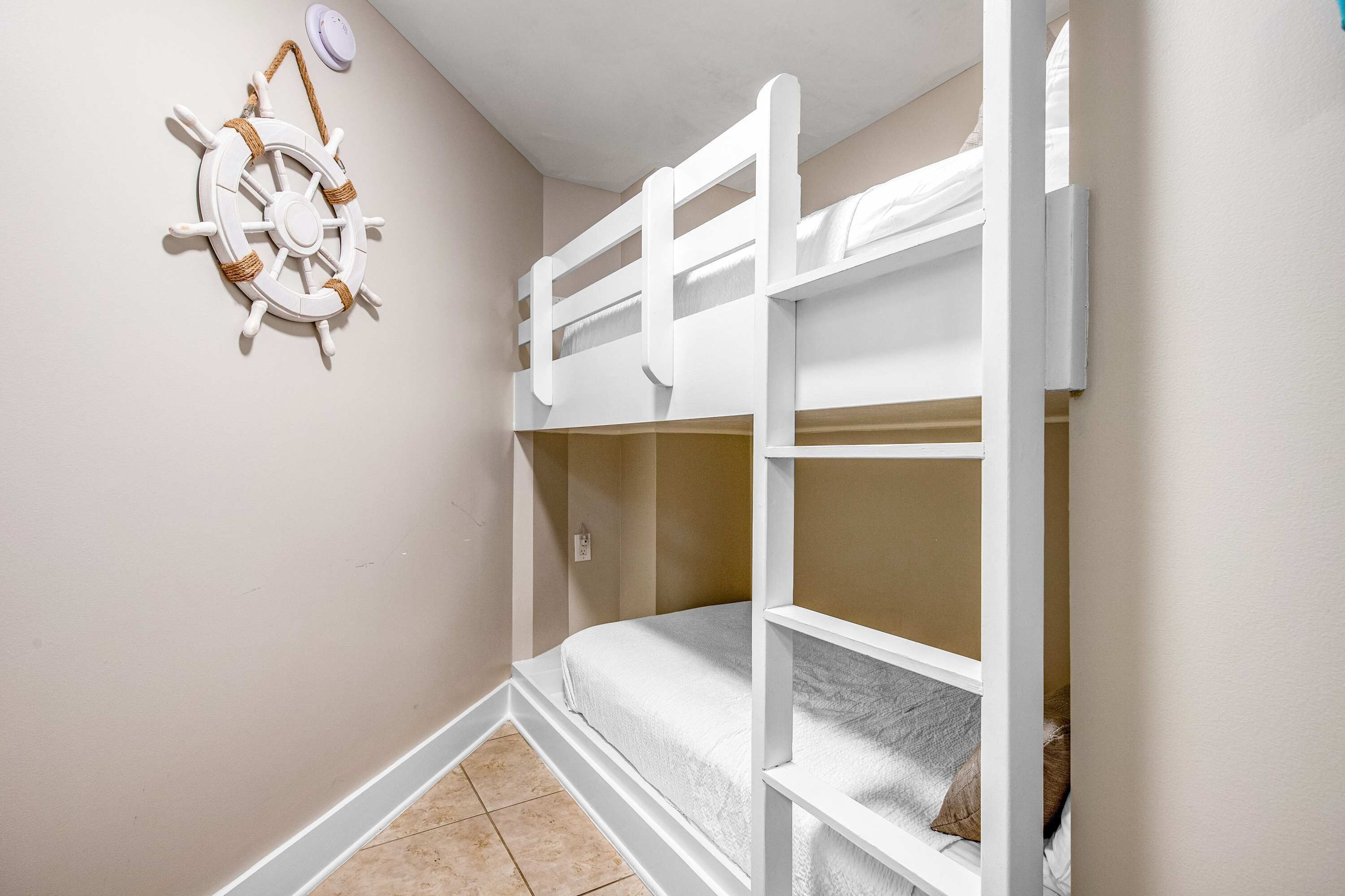 A bunk bed room with a ship's wheel decoration on the wall.