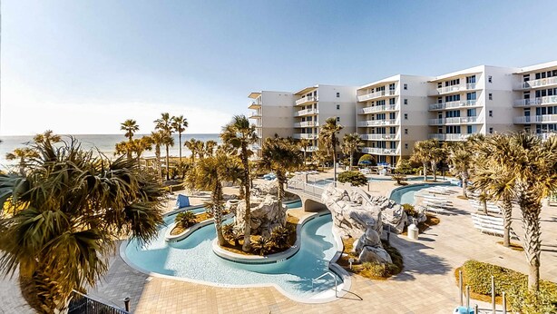 A resort with a pool area, palm trees, and a building with balconies. - 3rd Floor Picturesque Condo On Okaloosa Island Waterfall, Lazy River (Fort Walton Beach)