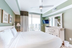 A hotel room with a large bed, a ceiling fan, a TV, a dresser, and a balcony with curtains. - Elegant, Spacious Condo At Waterscape Children's Playground, 2 Hot Tubs (Fort Walton Beach)