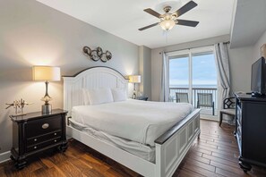 A bedroom with a bed, two bedside tables, a ceiling fan, a large window with curtains, and a TV. - Welcoming waterfront condo with a furnished balcony, pool & pool spa (Panama City Beach)