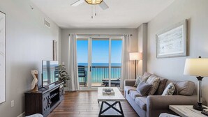 A living room with a television, sofa, coffee table, and a balcony with a view. - Welcoming waterfront condo with a furnished balcony, pool & pool spa (Panama City Beach)
