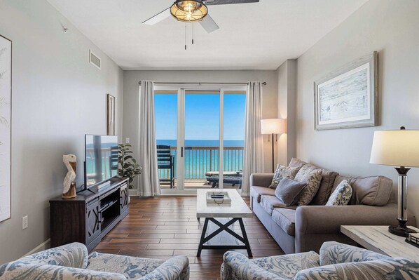 A living room with a television, sofa, coffee table, and a balcony with a view. - Welcoming waterfront condo with a furnished balcony, pool & pool spa (Panama City Beach)