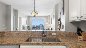 A kitchen with granite countertops, a stainless steel sink, and white cabinetry. - Welcoming waterfront condo with a furnished balcony, pool & pool spa (Panama City Beach)
