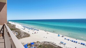 A beach view from a balcony with a clear sky, sandy beach, and umbrellas. - Welcoming waterfront condo with a furnished balcony, pool & pool spa (Panama City Beach)