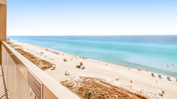 Une vue sur la plage depuis un balcon, avec un ciel dégagé, une plage de sable et l’océan.