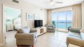 Un salon spacieux avec une grande télévision, deux canapés à motifs, une petite table et un balcon offrant une vue sur la mer.