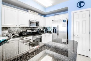 A modern kitchen with white cabinets, stainless steel appliances, and a granite countertop. - Inviting 11th-floor, beachfront condo with pool, hot tub & beach access (Panama City Beach)
