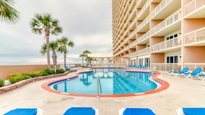 Un espace piscine avec des chaises longues bleues, des palmiers et un bâtiment doté de balcons.