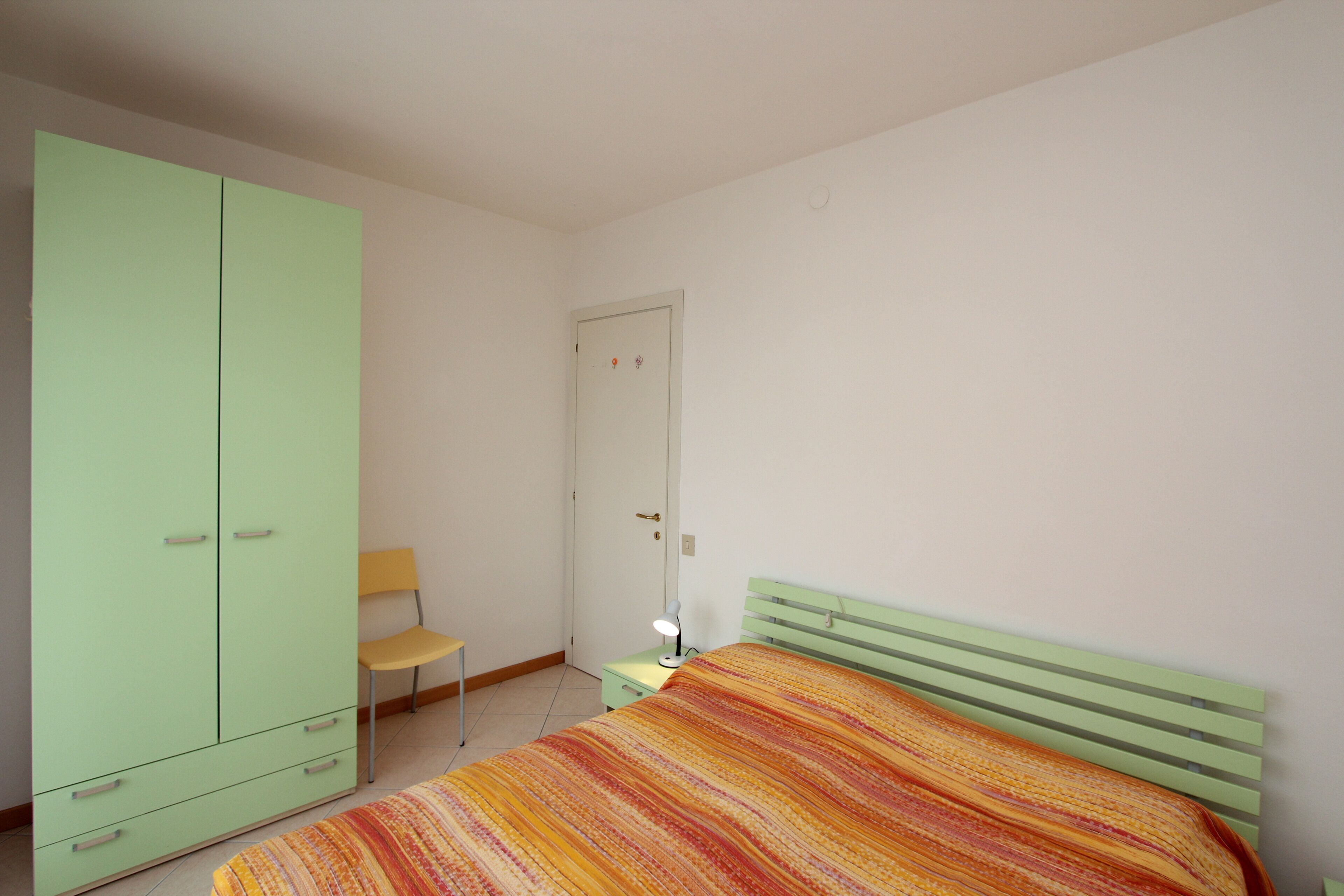 Una camera da letto con un letto, un armadio verde, una sedia e un comodino con una lampada.