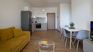 A modern living room with a yellow sofa, a glass coffee table, and a dining area with a white table and grey chairs. - Sea view -Blue Wave Two (Durrës)