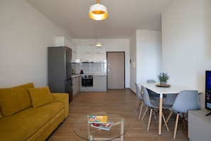 A modern living room with a yellow sofa, a glass coffee table, and a dining area with a white table and grey chairs. - Sea view -Blue Wave Two (Durrës)