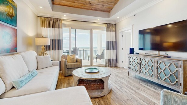 A spacious living room with a wooden ceiling, a large flat-screen TV, a sofa, a coffee table, and a balcony with curtains. - Oceanfront condo with balcony, lagoon pool, hot tub, & pickleball (Panama City,)