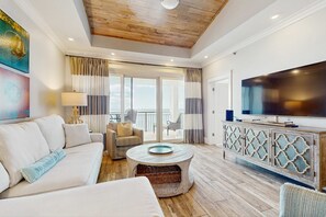 Un salón amplio con techo de madera, un televisor plano grande, un sofá, una mesa de centro y un balcón con cortinas.