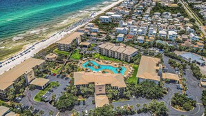 An aerial view of a coastal resort with beachfront properties, a central swimming pool, and a parking area. - Oceanfront condo with balcony, lagoon pool, hot tub, & pickleball (Panama City,)