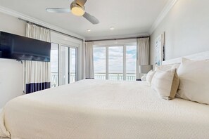 Ein großes Bett mit einem flachbildfernseher an der Wand, einem Deckenventilator und einem Balkon mit Vorhängen.