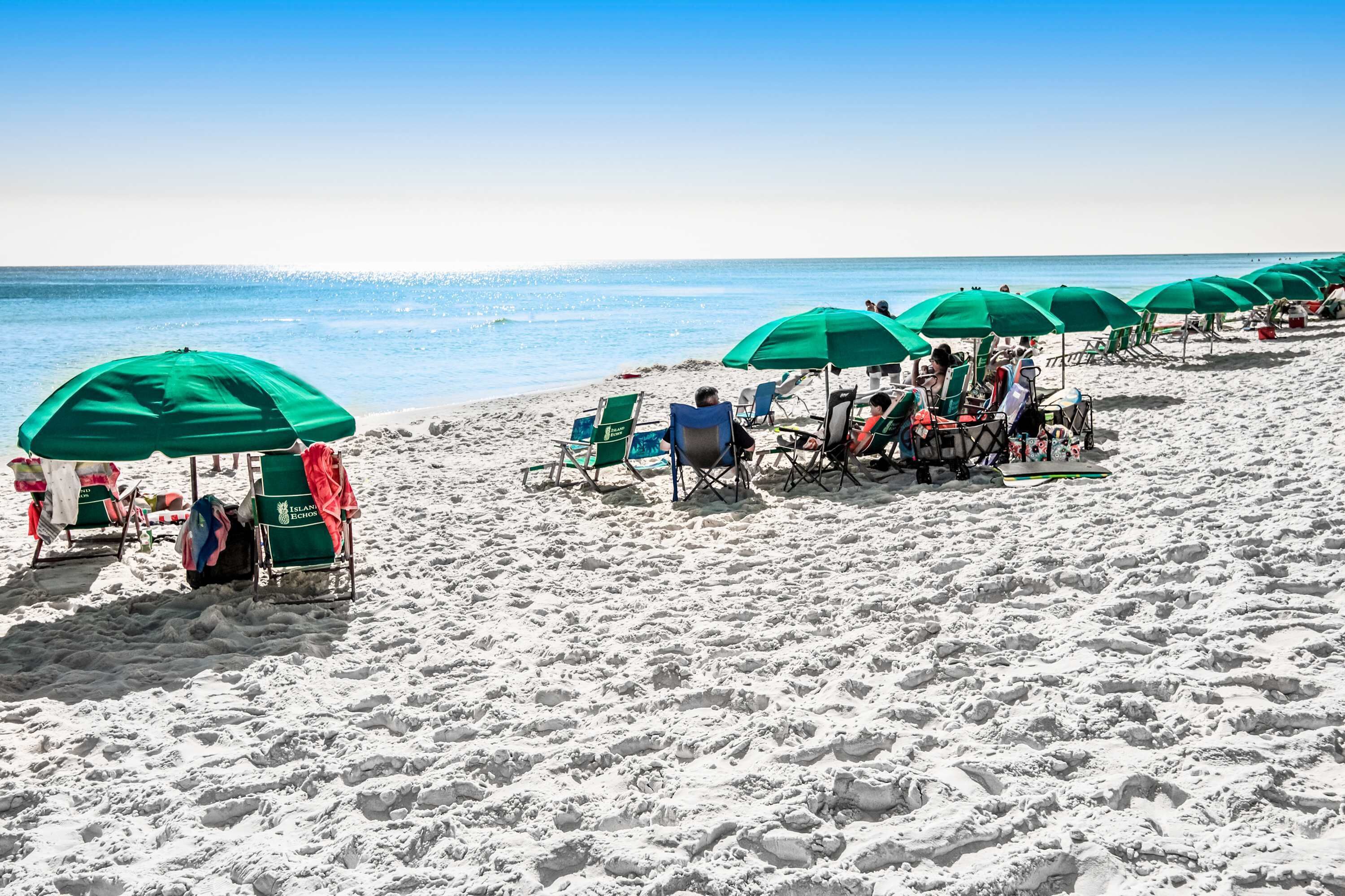 A beach with rows of green umbrellas and beach chairs.