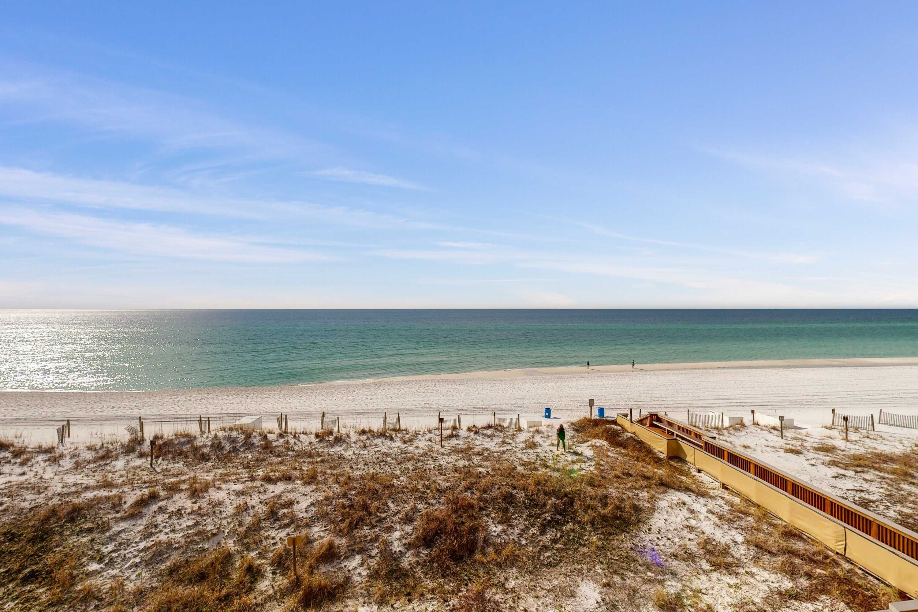 A beach with a sandy shore, a wooden boardwalk, and a clear blue sky.