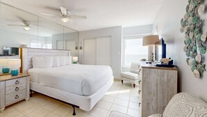 Une chambre à coucher comprenant un grand lit, une table de chevet, une commode, une chaise, un ventilateur de plafond et un élément décoratif mural.