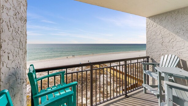 Un balcon donnant sur la plage, avec une balustrade et deux chaises vertes.