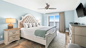 A bedroom with a bed, nightstands, a dresser, a ceiling fan, a TV, and a window with curtains. - Oceanfront condo with pool, ocean view, washer&dryer, & high-speed WiFi (Fort Walton Beach)