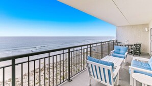 A balcony with a view of the ocean, white furniture, and a table with chairs. - Oceanfront condo with pool, ocean view, washer&dryer, & high-speed WiFi (Fort Walton Beach)