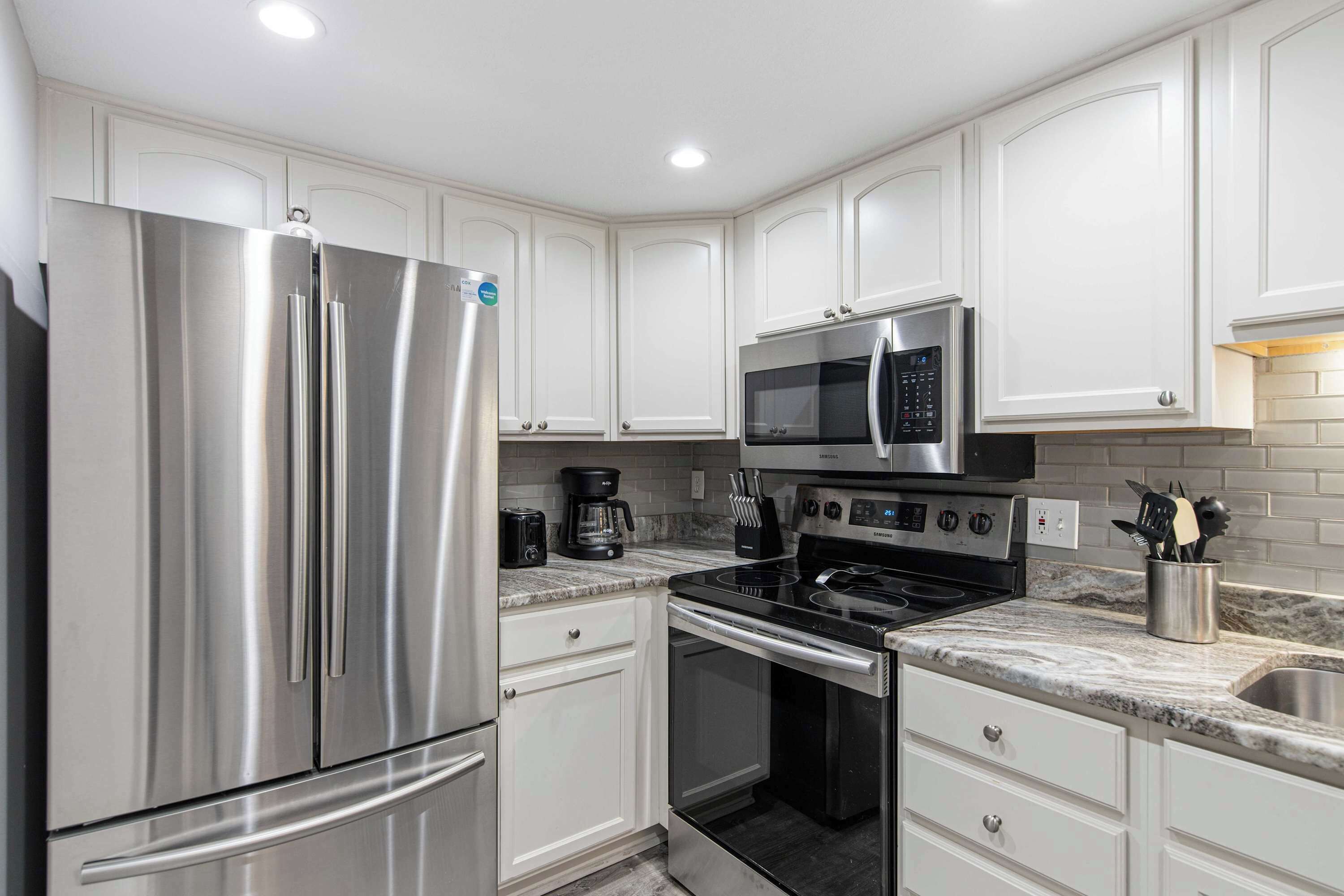 A modern kitchen with stainless steel appliances, white cabinetry, and a granite countertop.