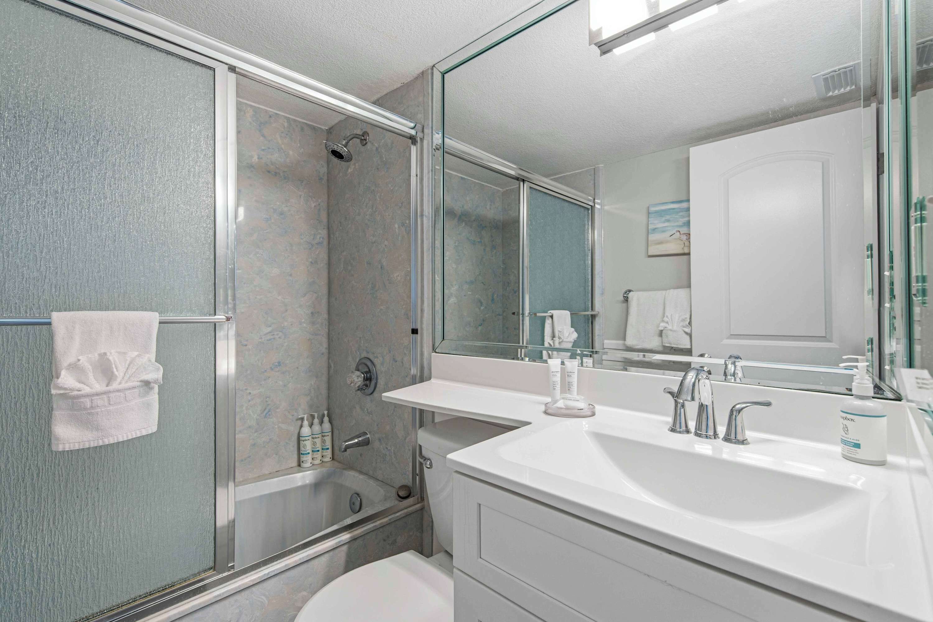 A modern bathroom with a glass shower enclosure, a white sink with two faucets, and a large mirror.