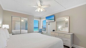 Een slaapkamer met een bed, een dressoir, een plafondventilator, een televisie en een grote spiegel.