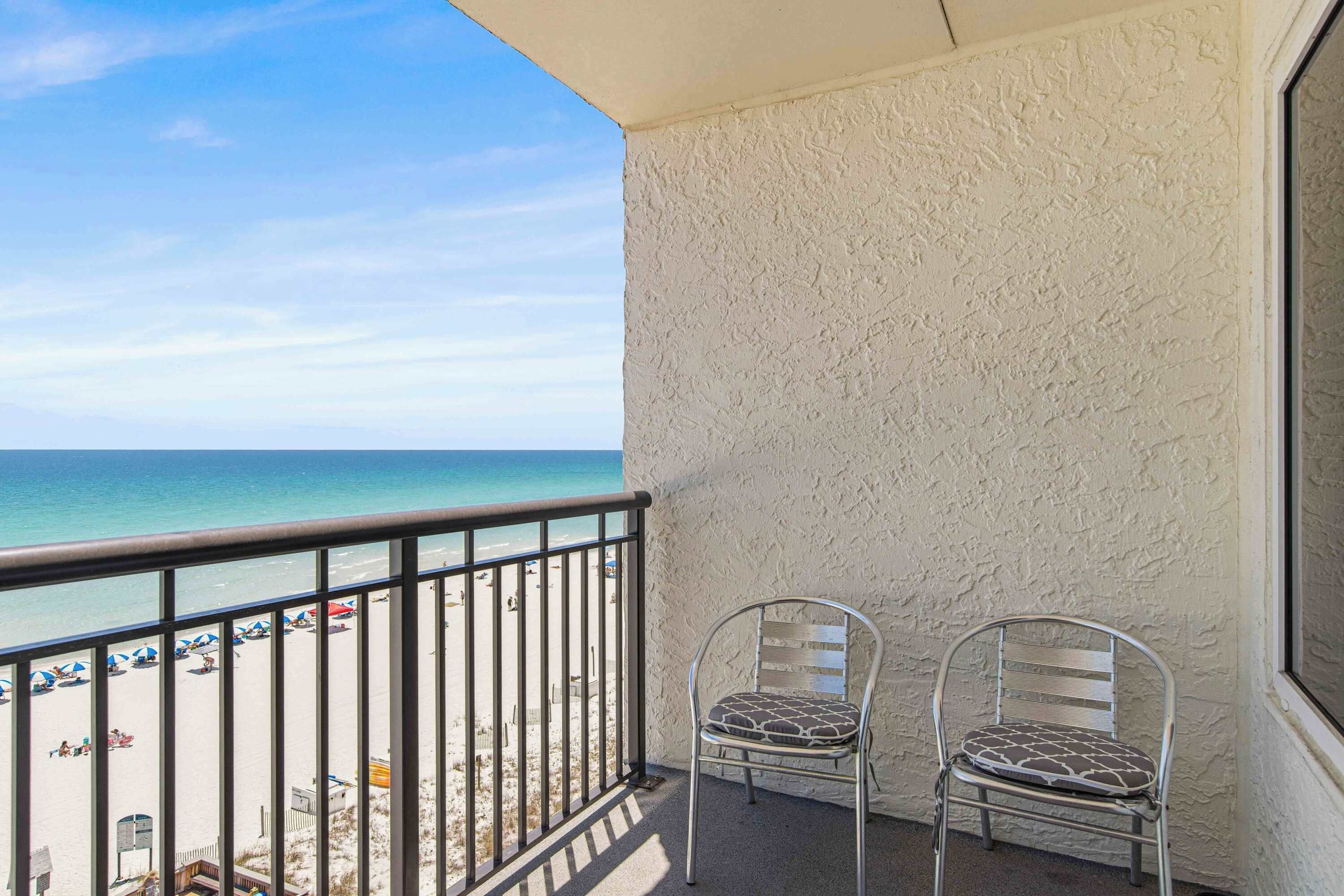 Ein Balkon mit Blick auf den Strand, einem Metallstuhl und einer weißen, strukturierten Wand.