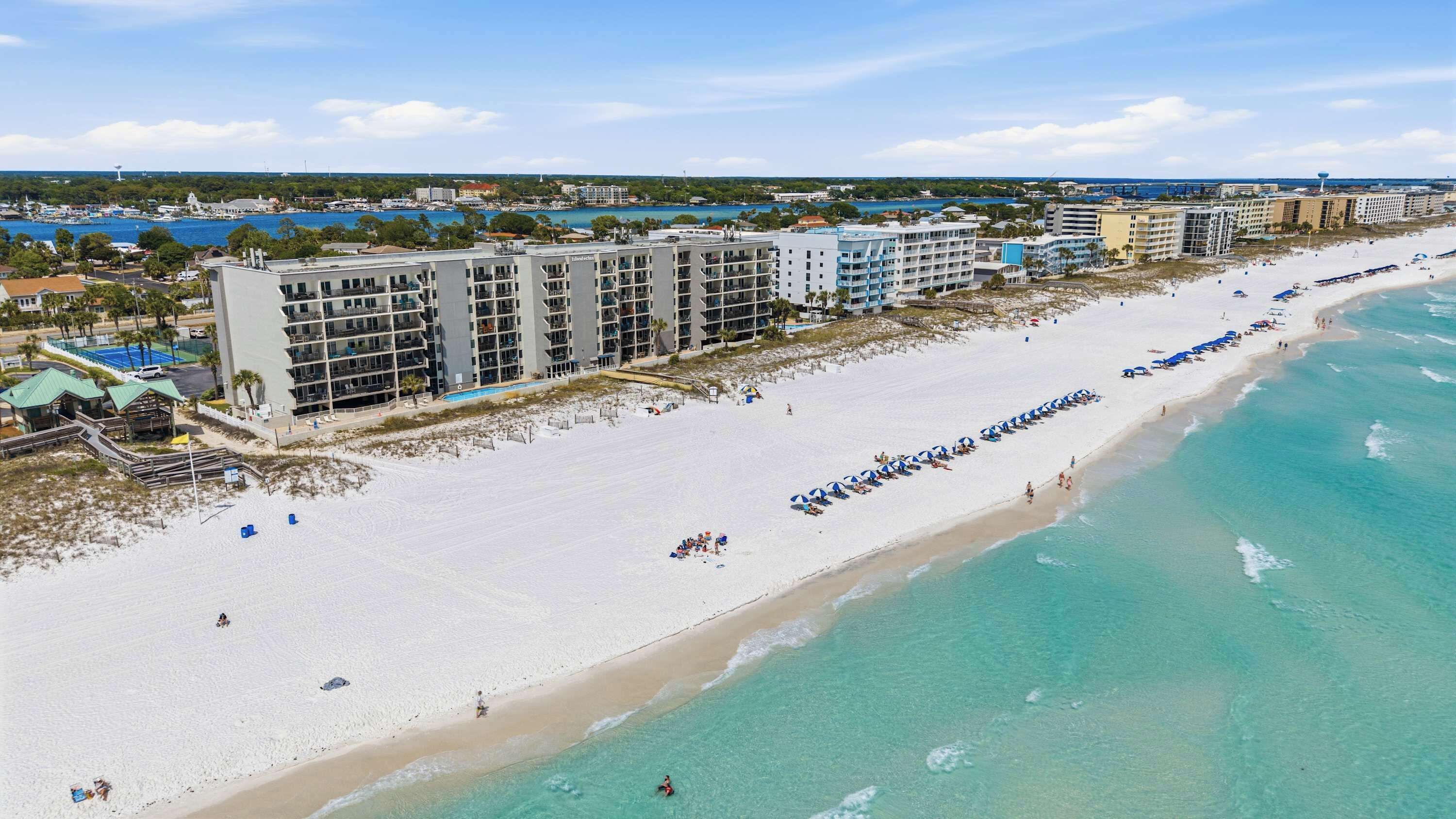 A beachfront hotel with multiple floors, a sandy beach, and clear turquoise waters.