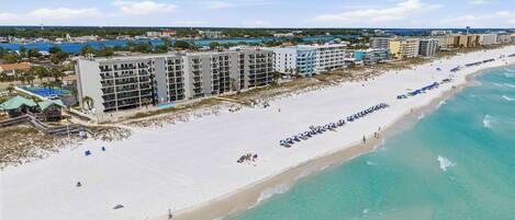 A beachfront hotel with multiple floors, a sandy beach, and clear turquoise waters.