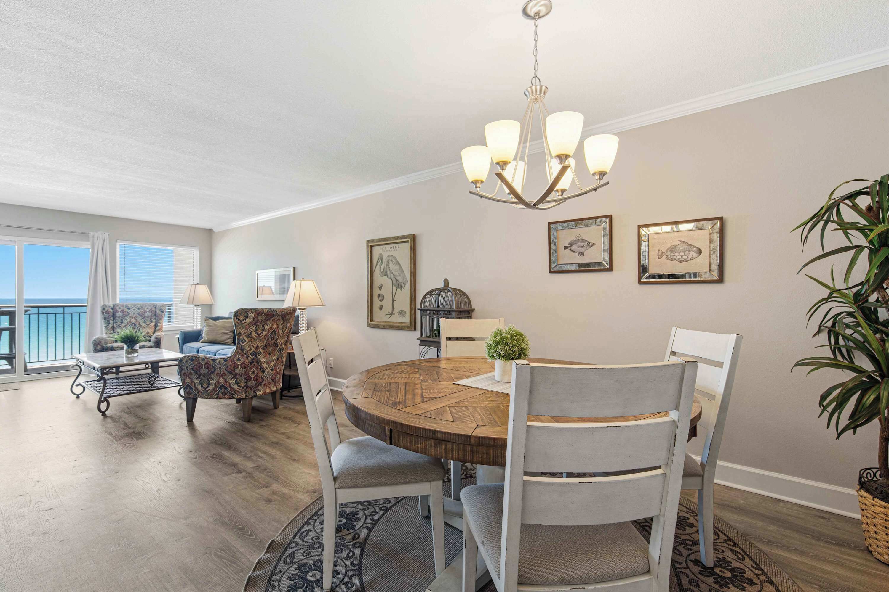 Un coin repas avec une table ronde en bois, des chaises blanches, un lustre et des œuvres d’art encadrées accrochées au mur.