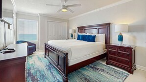 A bedroom with a large bed, a desk, a chair, a dresser, a ceiling fan, and a window with blinds. - Platinum penthouse with balcony views, pool, tennis court & beach access (Fort Walton Beach)